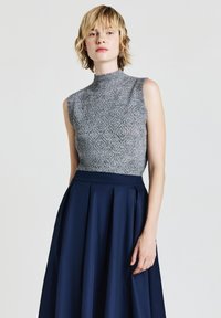 Graues ärmelloses Stricktop mit hohem Kragen, kombiniert mit einem marineblauen Faltenrock. Das Top zeichnet sich durch ein strukturiertes, offen gewebtes Muster aus.