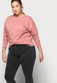 Pink sweatshirt with a crew neck and long sleeves, paired with dark gray fitted jeans. The fabric appears soft with a slight sheen.