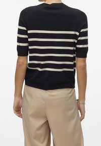 Czarny i kremowy sweter w paski z krótkim rękawem oraz okrągłym dekoltem, wykonany z miękkiego materiału, noszony z jasnobeżowymi spodniami.