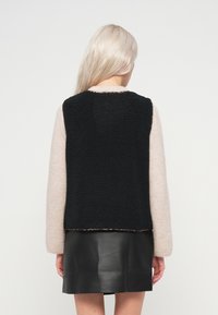 Μαύρος υφασμάτινος γιλέκο χωρίς μανίκια με ροζ μακριά μανίκια, πάνω από μια μαύρη δερμάτινη φούστα. Διαθέτει μαλακό, άνετο ύφασμα και στρογγυλή λαιμόκοψη.