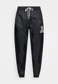 Svarta, lätta, vattenavvisande joggers med elastisk midja och dragsko. Har vit logotryck och smalnande mudd. Slät textur.