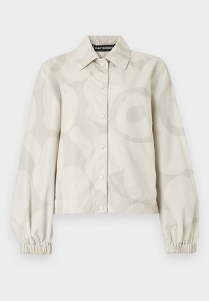 Jachetă bej cu nasturi, manșete elastice lungi și un model floral mare subtil, guler clasic și etichetă Marimekko pe interiorul gâtului.