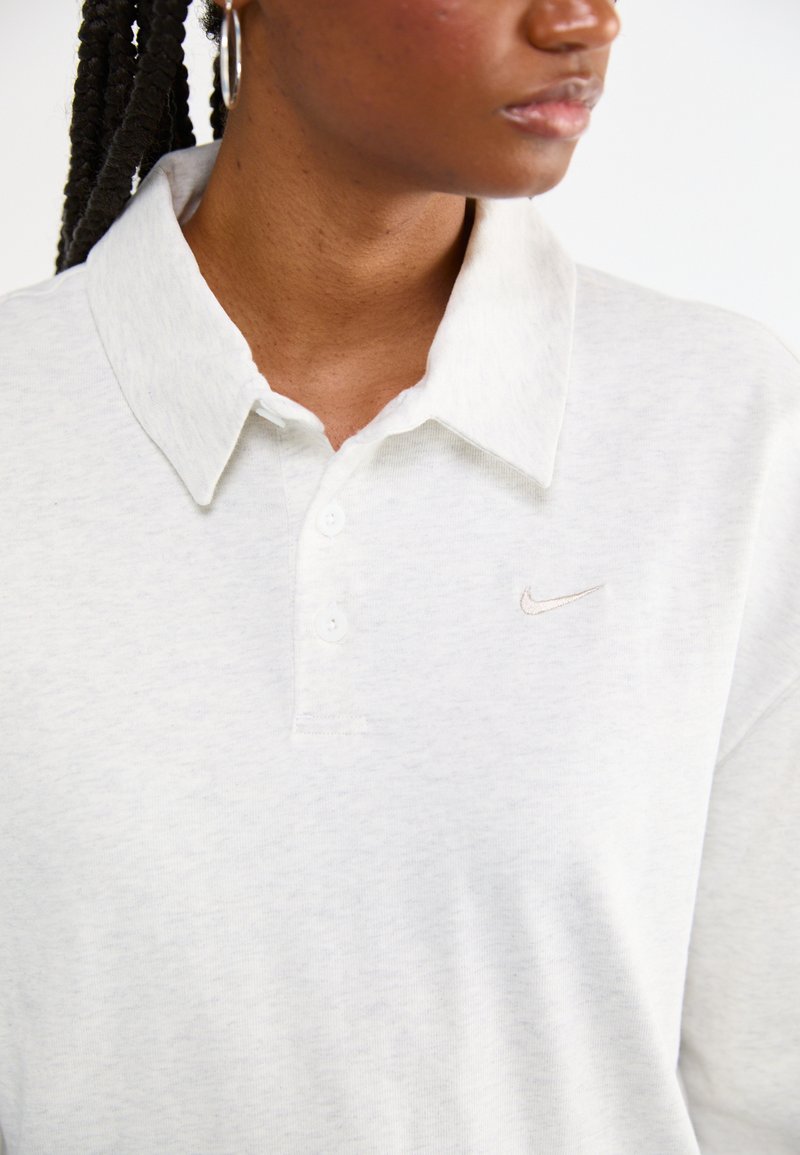 Polo gris clair en tissu doux, doté d'un col, de trois boutons et d'un petit logo brodé en beige.