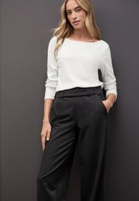 Top blanco de manga larga con escote barco, combinado con pantalones de talle alto en color carbón que presentan grandes botones decorativos y bolsillos laterales.