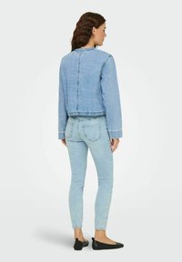 Veste en denim bleu clair à design court, manches longues et détails de couture au dos, assortie à un jean skinny bleu clair et des ballerines noires.