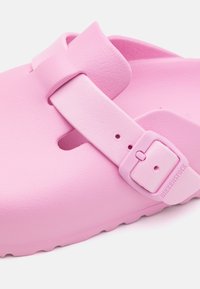 Rosa Birkenstock-sandal med slät syntetisk material, bred justerbar rem med spänne och en formad sula med texturerat grepp.