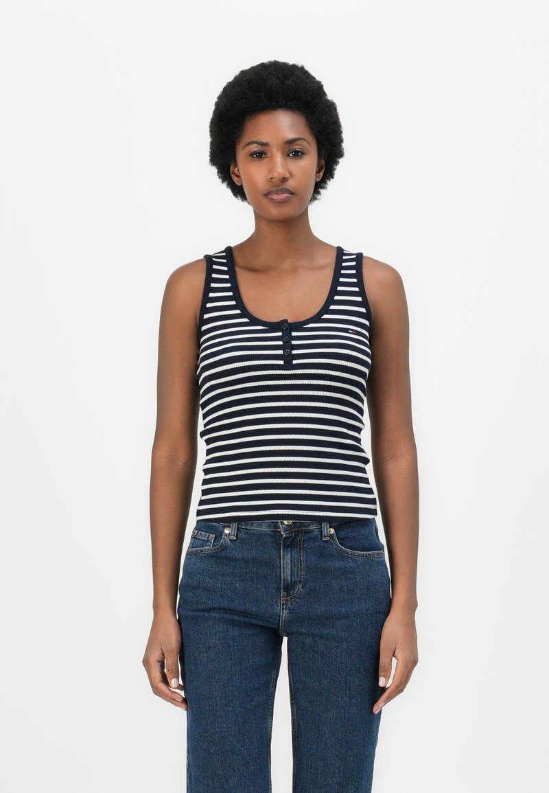 Camisola de alças riscada em azul-marinho e branco, com decote em forma de canoa e detalhe de três botões, usada com jeans de ganga escura de cintura alta.