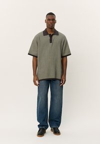 Strikket kortermet polo skjorte med ribbet tekstur, grønne og svarte striper, og en mørk krage. Kombinert med vide denimjeans.