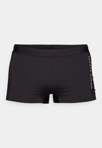 Shorts de bain noirs en tissu lisse et extensible. Dotés d'une taille mi-haute et de jambes courtes ; logo imprimé en blanc sur le côté.