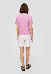 Roze katoenen t-shirt met korte mouwen, gecombineerd met witte linnen short en zwarte platform sandalen, gezien vanachter.