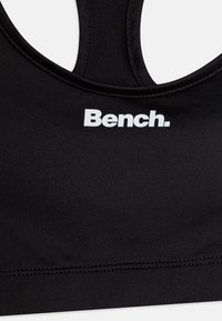 Svart sports-bh med rund halslinning, laget av glatt stoff. Har en hvit logo "Bench." på forsiden. Enkel design uten pynt.