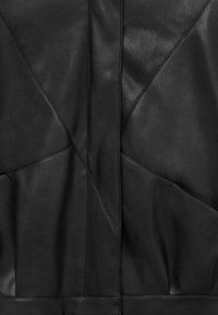 Tissu en cuir noir avec des panneaux géométriques cousus formant des formes angulaires et des coutures.