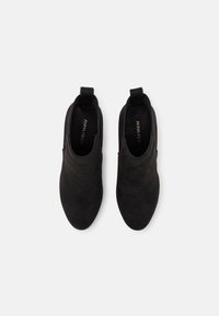 Bottines en daim noir avec une texture lisse, bout arrondi et panneaux élastiques sur les côtés. Comprend une languette pour un enfilage facile.