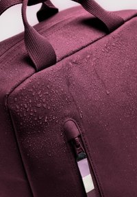  Bordeaux kleurige duffelbag met waterdruppels, voorzien van textuurstof, dubbele handvatten en een zijvak met rits met een gestreepte trekband.