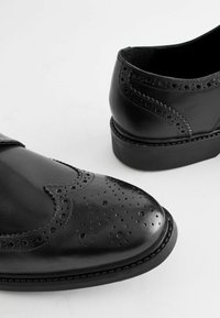 Chaussures en cuir noir avec des détails en brogue, une finition lisse, un bout rond et un petit talon en caoutchouc. Le design comprend des accents perforés.
