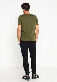 Vihreä oliivinvärinen istuva t-paita lyhyillä hihoilla, yhdistettynä mustiin jogger-housuihin, joissa on joustavat hihansuut ja sileä, kevytnesteinen kangas.