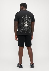 Black t-shirt featuring a white eye design on the back, short sleeves, and a round neckline, paired with black shorts and sneakers.