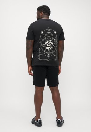T-shirt noir avec un design d'œil blanc au dos, à manches courtes et col rond, associé à un short noir et des baskets.