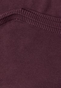 Gros plan d'un col côtelé doux sur un pull en tricot violet foncé montrant la texture et les détails du tissu.