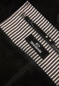 Wnętrze z czarnego zamszu z czarno-białą, paskowaną podszewką. Zawiera kieszeń na zamek oraz metkę z nazwą marki w białym napisie.