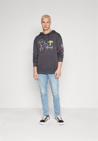 Dark gray hoodie with graphic print, front kangaroo pocket, paired with light blue jeans and black sneakers featuring white soles.