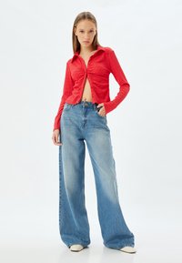 Rød tekstureret langærmet skjorte med knaplukning foran og cropped snit, parret med lys blå oversized denim jeans. Skoene er off-white.