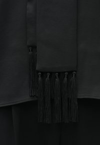 Čierna textília s hladkým povrchom a strapcami na leme. Tkanina má matný povrch, čo zdôrazňuje čistý dizajn a minimálne ozdoby.