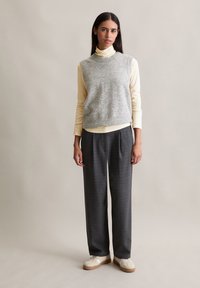 Pull en laine gris sans manches sur un col roulé jaune pâle, associé à un pantalon à carreaux gris et des baskets crème. Design simple et soigné.