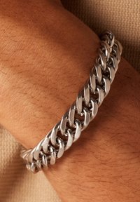 Zilveren armband met ronde schakels, met een gepolijste afwerking tegen gebruinde huid, die de zachte textuur en het ontwerp benadrukt.