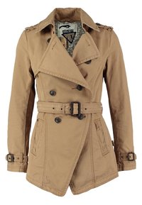 Trench-coat beige à double boutonnage avec larges revers, taille et poignets ceinturés, deux poches latérales et doublure intérieure à motifs visible au col.