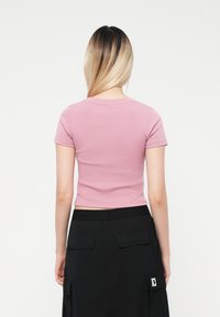 Prikladna, kratka majica s kratkim rukavima od mekane pastelno ružičaste pamučne tkanine. Ovratnik je okrugli, sa glatkim završetkom i minimalnim šavovima. Nositi uz crne cargo hlače.