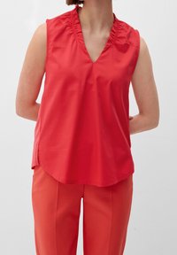 Blusa roja sin mangas con escote en V y un cuello con volantes, hecha de una tela suave; combinada con pantalones rojos a juego.