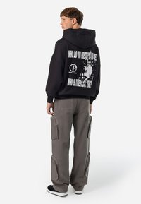 Black sweatshirt with white text on the back, paired with gray cargo pants featuring multiple zippered pockets and black sneakers.