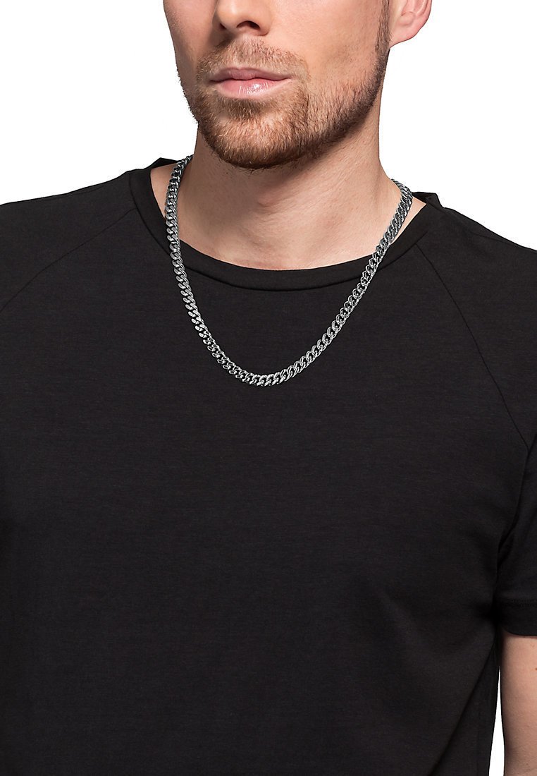 Collana in argento con link spessi e intrecciati, indossata su una maglietta nera. La catena ha una finitura lucida che riflette la luce.