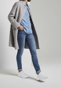 Grå överdimensionerad kappa, ljusblå skjorta med knappar, blå jeans och vita sneakers. Mjuk textur, avslappnad design och uppvikta jeans.