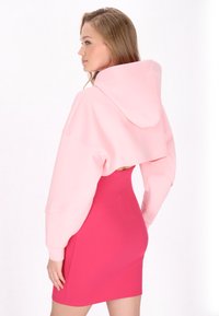 Rosa croppad hoodie med vida ärmar, parat med en figurnära ljusrosa ribbad klänning. Slät textur och livfulla färger som skapar en modern look.