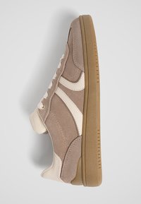 Baskets en daim beige avec des accents en cuir blanc et une épaisse semelle en gomme, vues de côté sur un fond blanc.