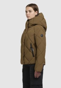 Gequilted bruine pufferjack met een capuchon, zijzak met rits en logopatch op de mouw. Textuur oppervlak en oversized pasvorm.