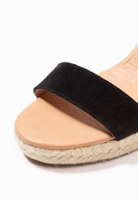 Sandalo in suede nero con una vasta fascia, soletta in pelle marrone chiaro e suola in juta intrecciata, con una finitura testurizzata e bordi lisci.
