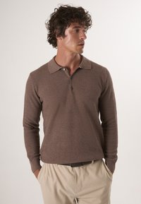 Bruine lange mouwen polo trui met een gestructureerd patroon en een kraaghalslijn, gecombineerd met lichtbeige broeken.