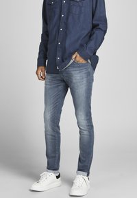 Ljust blå slim-fit jeans i denim, med slitna detaljer, femfickorsdesign, bärs med en mörk skjorta och vita sneakers.
