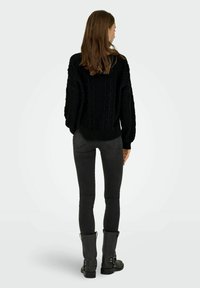 Pull en tricot noir avec un design texturé, associé à un jean skinny noir et des bottines noires avec des accents de boucle.
