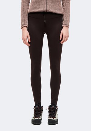 Un mannequin cadré partiellement porte un legging marron foncé à taille élastique avec cordon de serrage, un haut en polaire beige et des chaussures de randonnée noires.