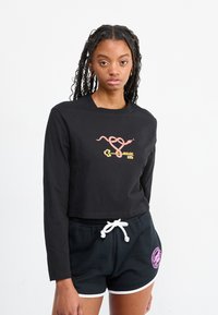 Maglietta nera a maniche lunghe e taglio corto con un design grafico colorato che presenta serpenti e chiavi. Abbinata a pantaloni corti neri con accenti bianchi.