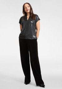 Svart topp med korta ärmar, glansig textur och v-ringning, kombinerad med lösa svarta sammetbyxor med rosettdekorer på fållen.