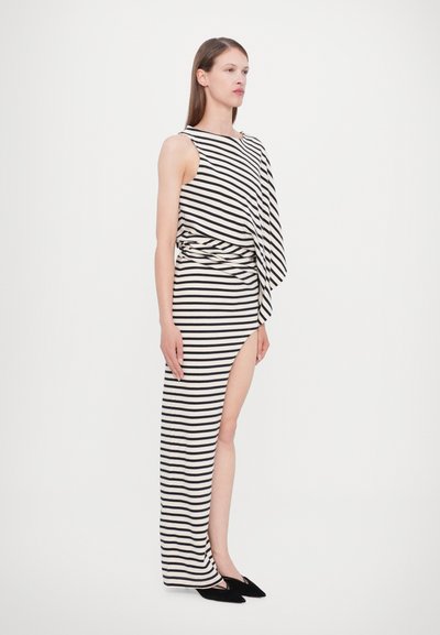 Striped dress with one shoulder design, featuring black and white stripes, side slit, and flowing fabric. Worn with black shoes.
