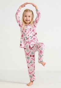 Pink pajama set featuring a button-up top and patterned pants with holiday motifs like bows, ornaments, and holly. Soft, lightweight fabric.