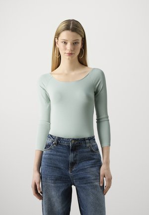 Light green long-sleeve bodysuit with a scoop neck, paired with high-waisted blue jeans featuring a faded texture and front pockets.