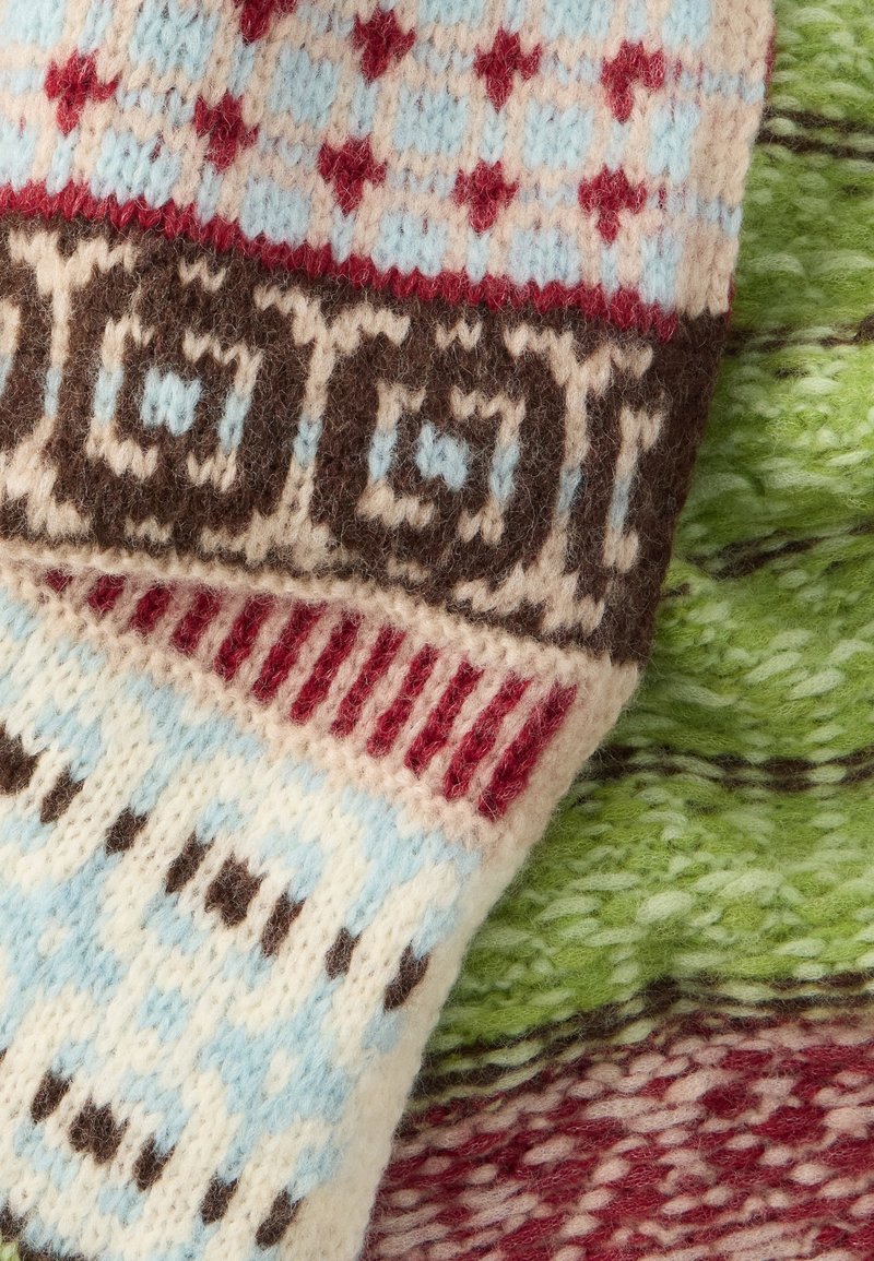 Colorful knitted fabric featuring patterns in blue, red, brown, and cream, with a soft texture and distinct geometric designs.