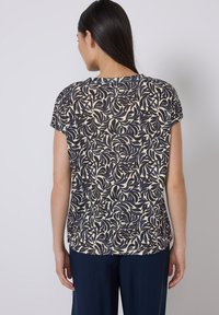 Kurzarmoberteil in Marineblau und Creme mit einem blättrigen Muster, aus weichem Stoff gefertigt, mit rundem Ausschnitt und leicht abgerundetem Saum.